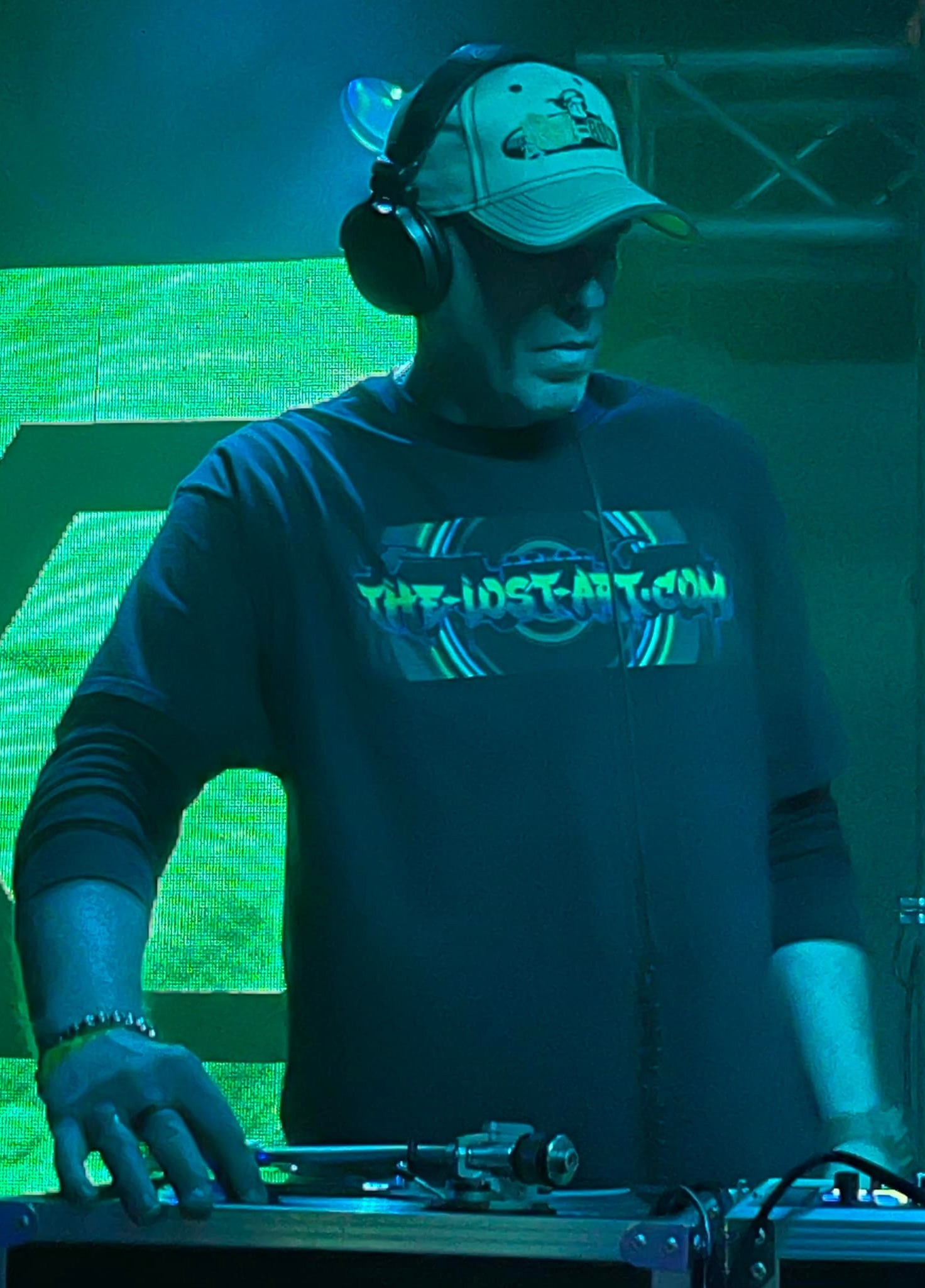 DJ Natural Nate® in The-Lost-Art.com long sleeve leaning on decks under pink and magenta stage lighting